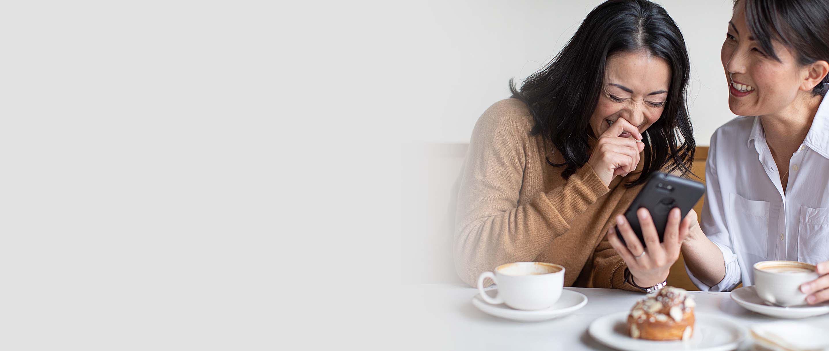 Two women laughing looking at a phone while drinking coffee