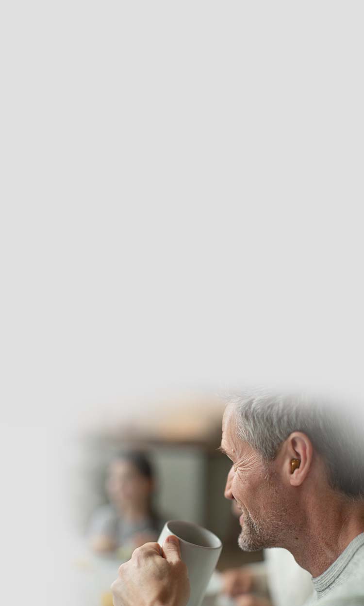 A man drinking coffee with a hearing aid in his ear