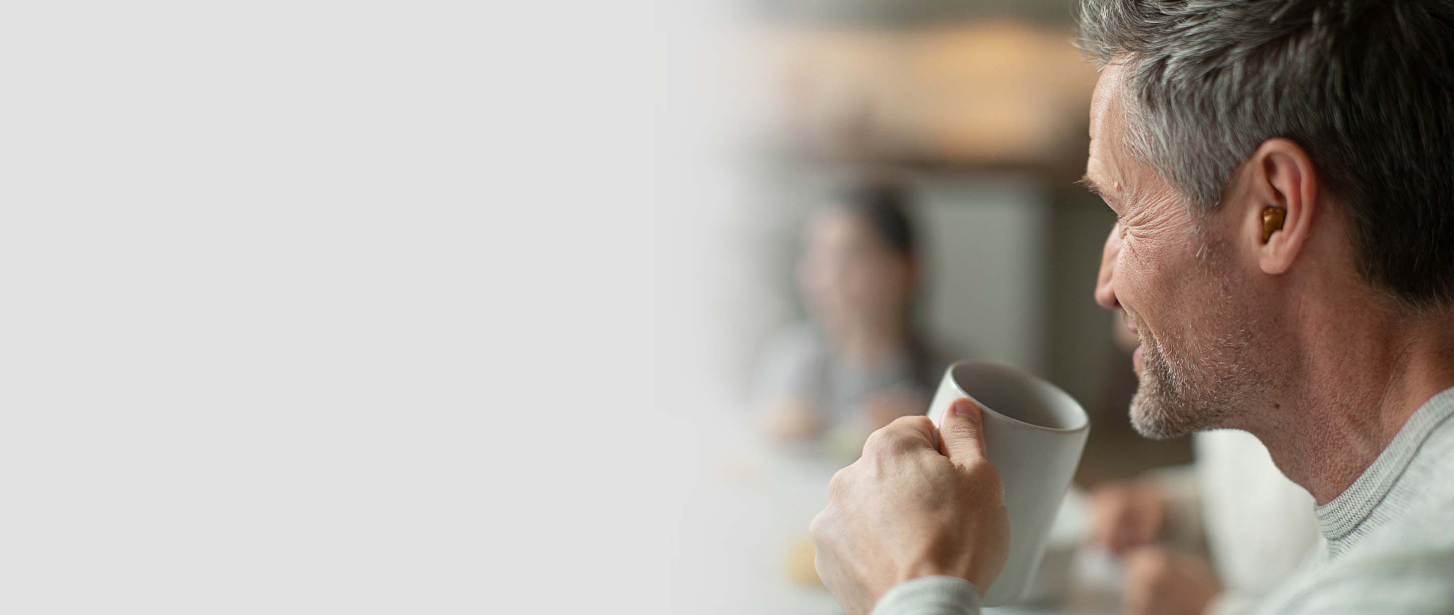 A man drinking coffee with a hearing aid in his ear