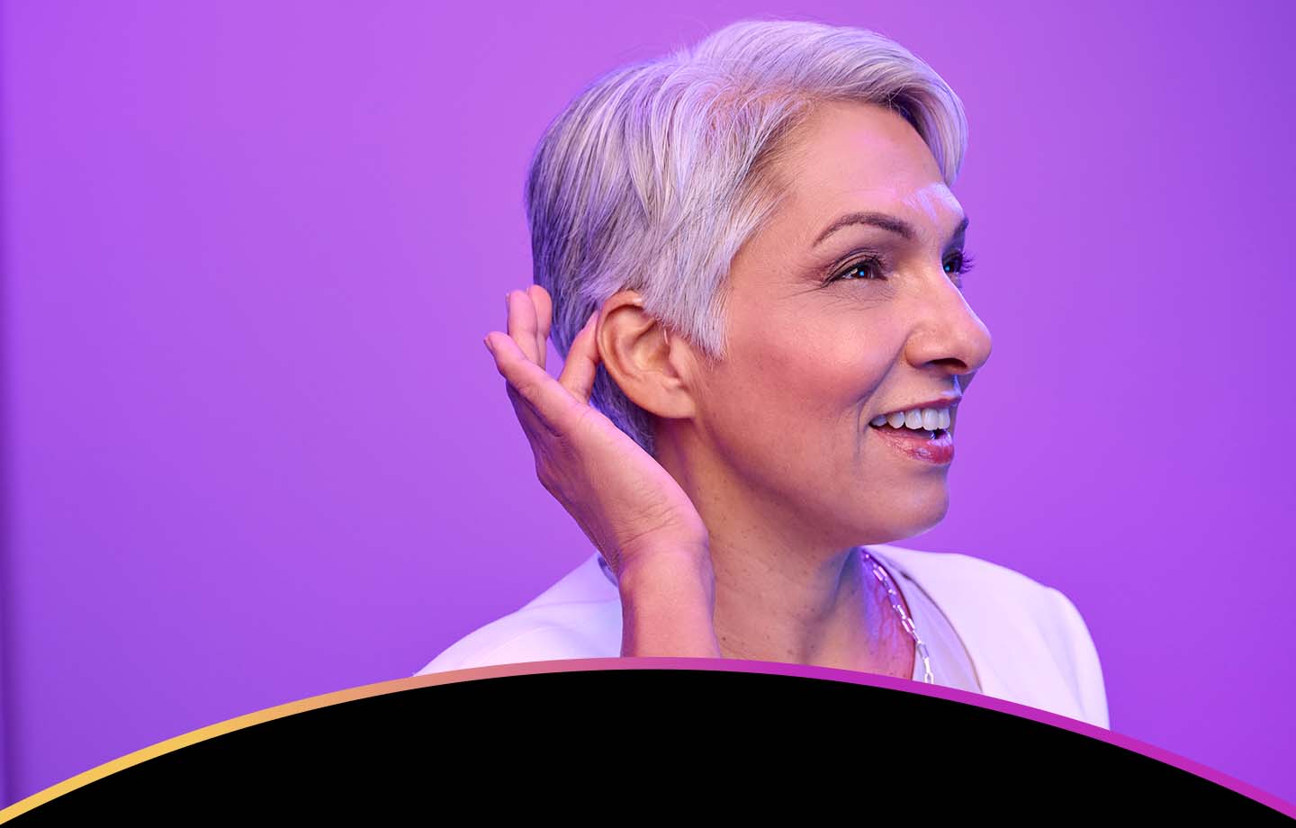 A smiling woman adjusting a hearing aid behind her ear